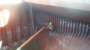Hold & Deck De-Scaling — Operator descaling the corrugated bulkhead of a bulk carrier.